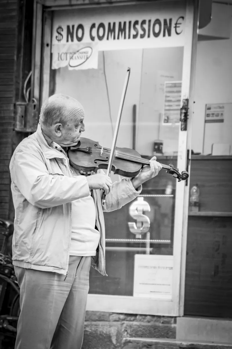 Older violinist playing on the street in front of a currency exchange kiosk